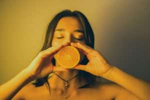 woman holding half an orange in her hands over her mouth