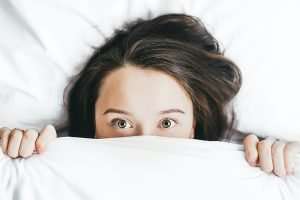 woman sleeping in white bed and sheets showing her eyes